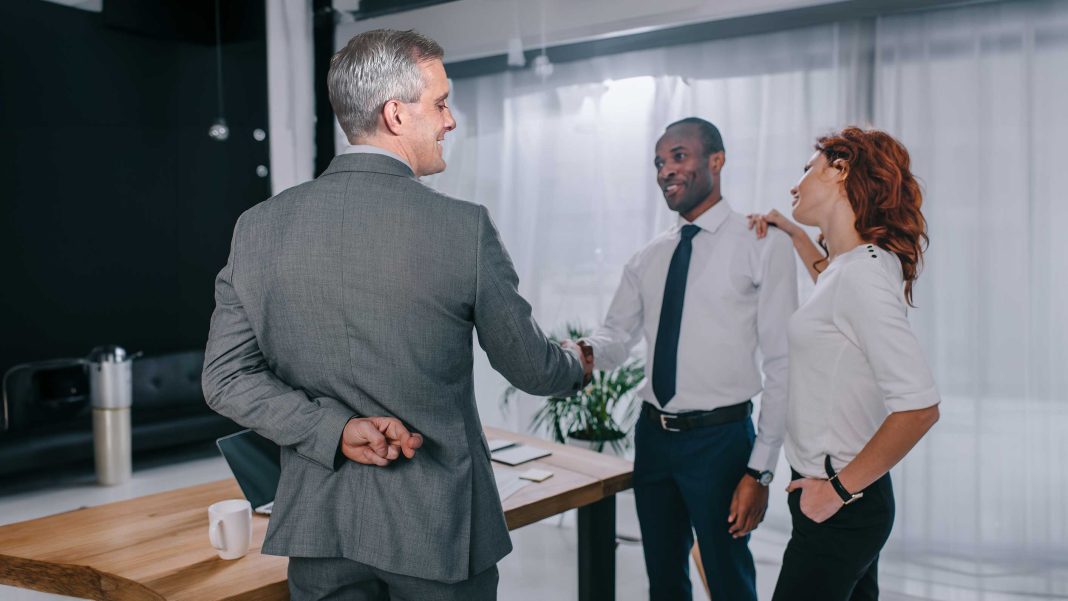 McDonough-Telework-Arbitration Telework Arbitration - Secretary McDonough is depicted shaking the hand of an employee, in this context he is agreeing to a telework plan, but he has his fingers crossed behind his back indicating a double cross.